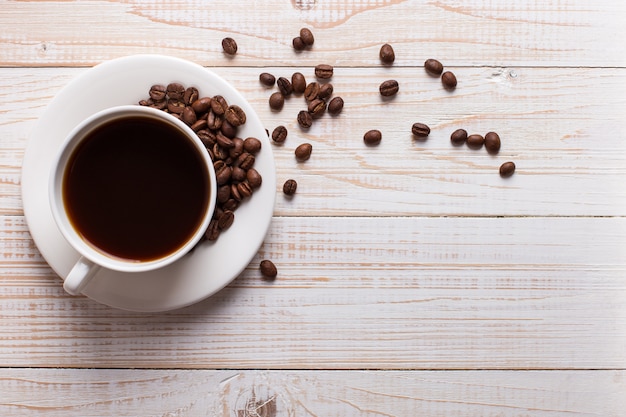 Xícara de café com grãos de café espalhados em um fundo de mesa de madeira. Humor de manhã de outono, copyspace.