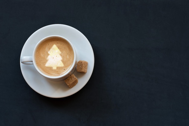 Xícara de café com leite, açúcar de cana e árvore de Natal em fundo escuro. Vista superior, copie o espaço.