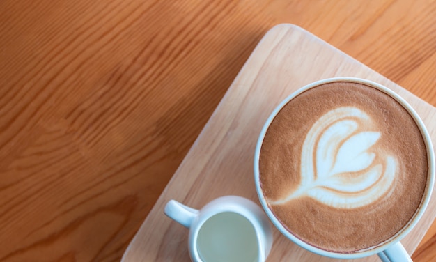 Xícara de café com leite com arte de latte na mesa de madeira na cafeteria.