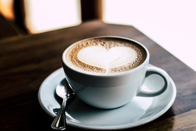 Xícara de café com leite com formato de coração em fundo de madeira velho ao sol da manhã