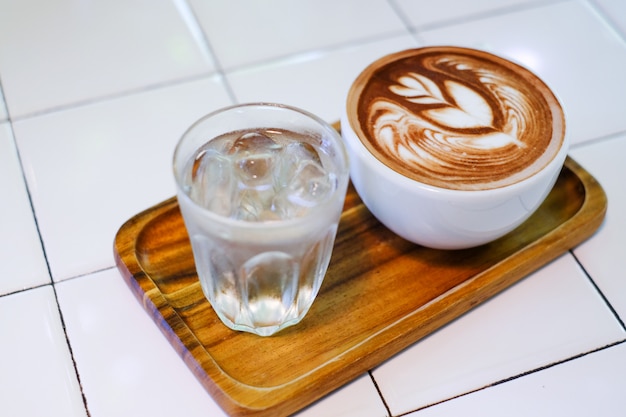 Xícara de café com leite na placa de madeira e água fria