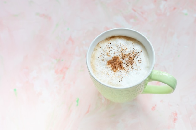 Xícara de café com leite temperado com canela na superfície rústica rosa claro. planta plana, vista superior, cópia espaço, conceito de bebida quente de inverno