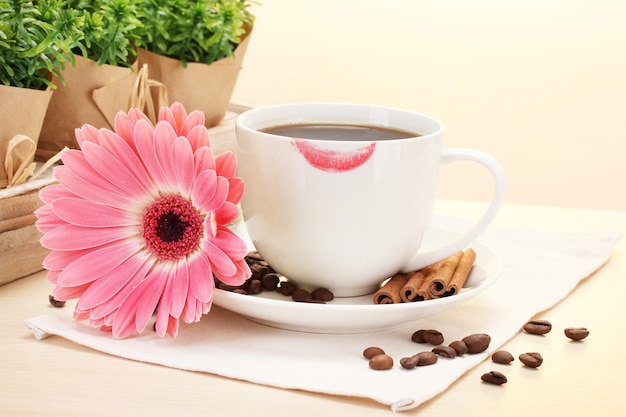 Xícara de café com marca de batom e paus de canela de feijão gerbera na mesa de madeira