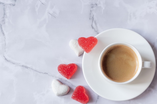 Xícara de café com marmelada na forma de um coração em um fundo de mármore.