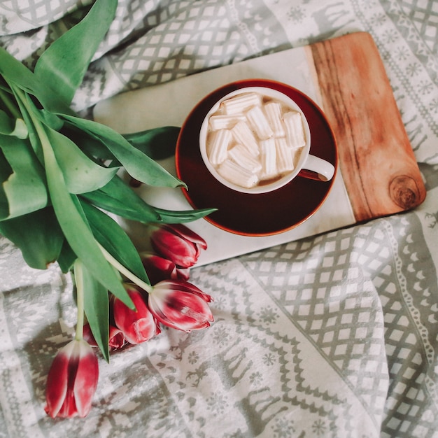 Xícara de café com marshmallows e tulipas vermelhas na cama. conceito de feriado, aniversário, dia dos namorados, 8 de março