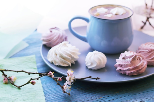 Xícara de café com merengue florescendo ramos de cereja em água em uma jarra de vidro doce sobremesa