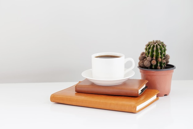 Xícara de café com notebook e cacto na mesa branca