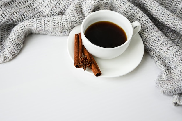 Xícara de café com paus de canela e estrela de anis em fundo branco. Suéter ao redor. Rotina matinal de inverno. Pausa para o café. Copie o espaço. Café da manhã.