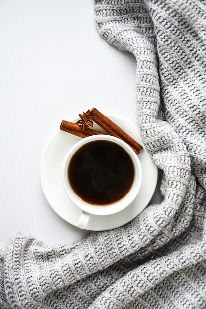 Xícara de café com paus de canela e estrela de anis em fundo branco. Suéter ao redor. Rotina matinal de inverno. Pausa para o café. Copie o espaço. Vista do topo. Café da manhã. Postura plana