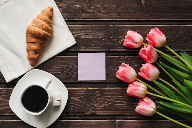 Xícara de café com um buquê de flores tulipa rosa e um croissant para a manhã