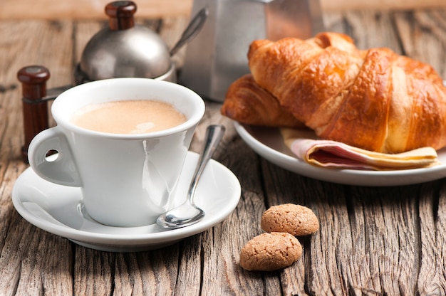 Xícara de café com um croissant café da manhã na mesa de madeira