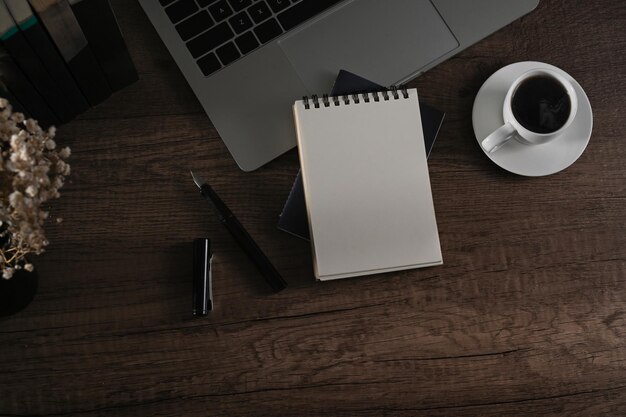 Xícara de café de computador portátil de bloco de notas vazio e vaso de flores na mesa de madeira Vista superior plana