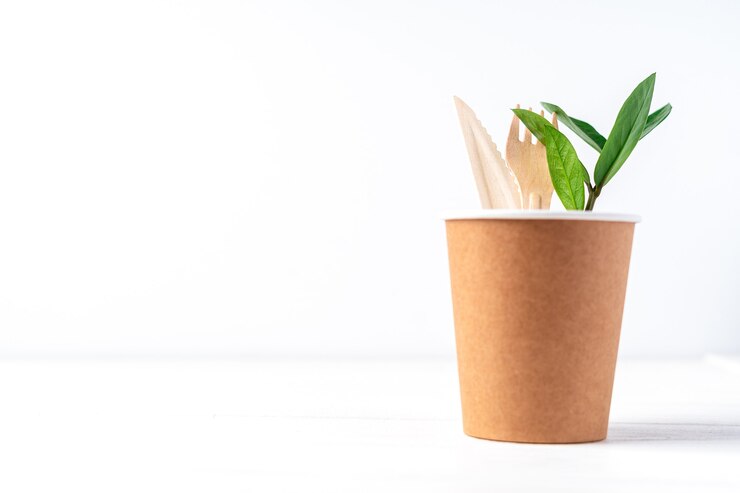 Foto xícara de café de papel artesanal, folhas verdes e talheres reciclados
