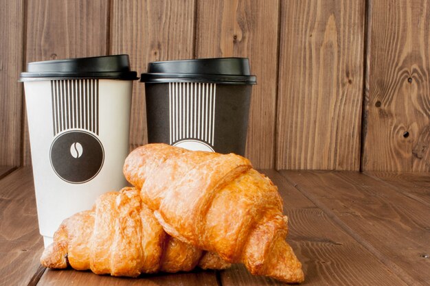 Xícara de café de papel e croissants em fundo de madeira