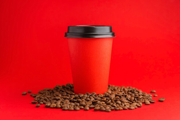 Xícara de café de papel vermelho para viagem com tampa preta em feijão torrado em fundo vermelho Mock up