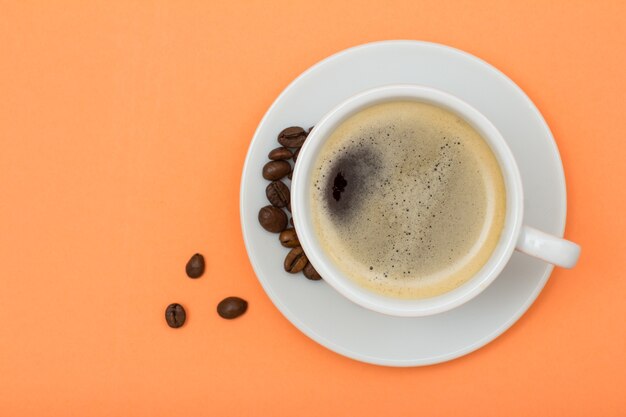 Xícara de café de porcelana branca em pires com grãos de café em fundo cor de pêssego. vista do topo