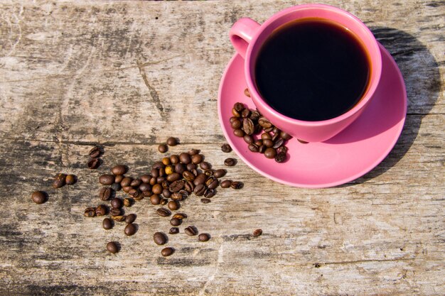 Xícara de café-de-rosa e grãos de café na mesa de madeira rústica. Vista do topo