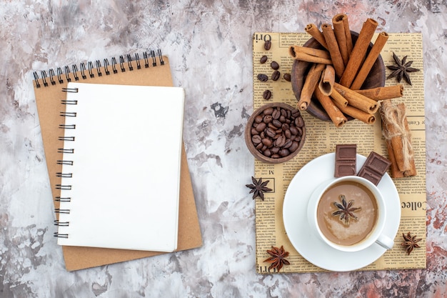 Foto xícara de café de vista superior com grãos de café torrados de erva-doce em uma tigela de madeira paus de canela de chocolate em uma tigela de anis em cadernos de jornal na mesa