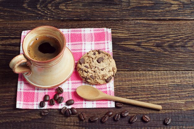 Xícara de café e biscoito com chocolate em um guardanapo vermelho colocado sobre uma mesa de madeira escura