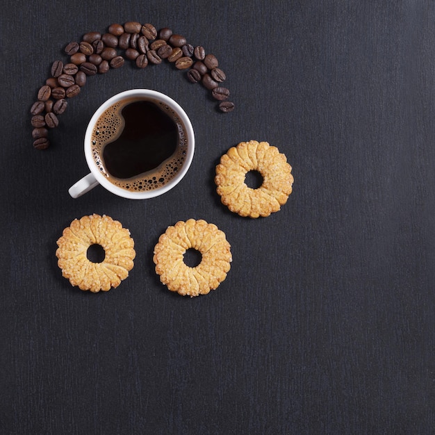 Xícara de café e biscoitos amanteigados na vista superior de fundo de pedra preta com espaço de cópia
