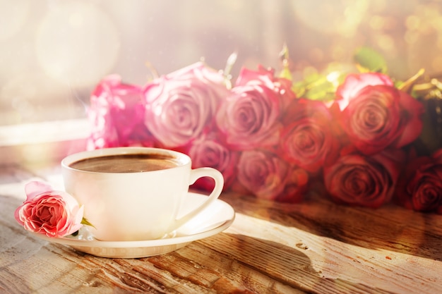 Xícara de café e buquê rosa rosas na mesa