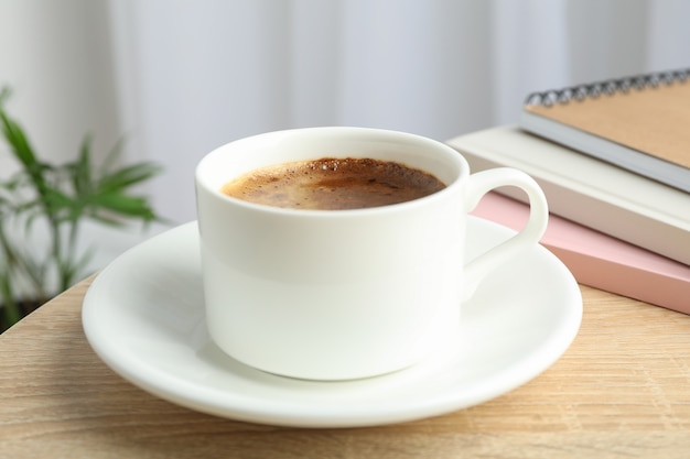 Xícara de café e cadernos na mesa de madeira contra a luz de fundo com plantas