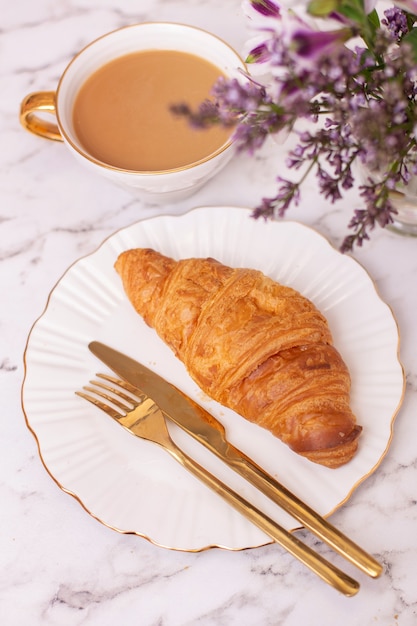 xícara de café e croissant com buquê de flores