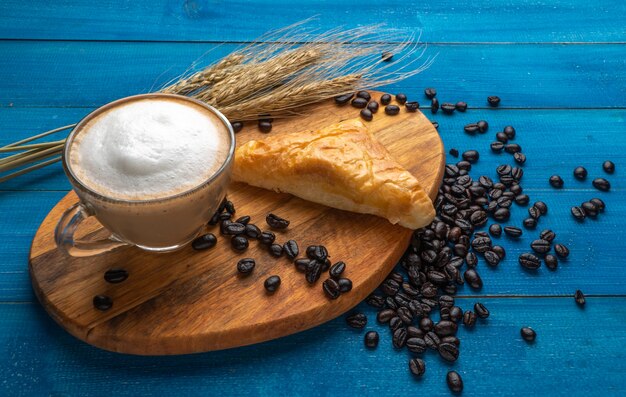 Xícara de café e croissant no café da manhã na superfície azul de madeira com grãos de café.