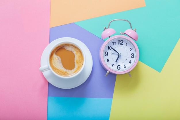 Xícara de café e despertador em fundo de papel pastel