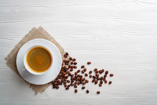 Xícara de café e feijão em uma mesa de madeira branca.