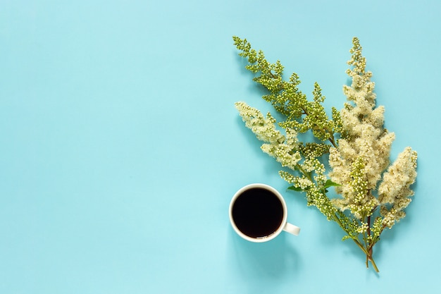 Xícara de café e flores desabrochando galho branco sobre fundo de papel azul