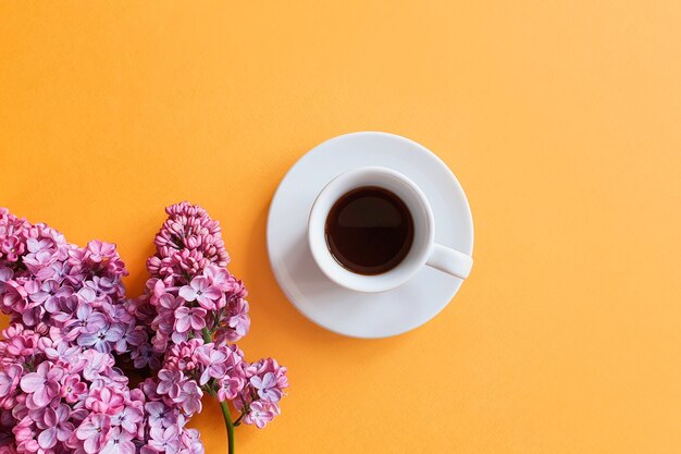 xícara de café e flores lilás na mesa amarela.