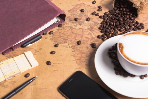 Foto xícara de café e grãos de café na mesa com fundo grande mapa na tabela de guia