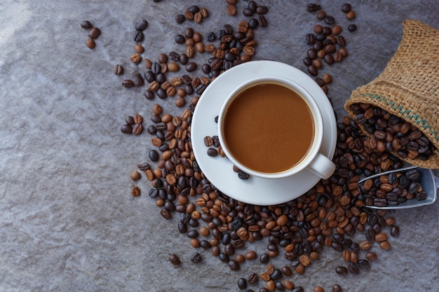 Xícara de café e grãos de café torrados em saco marrom, vista superior.