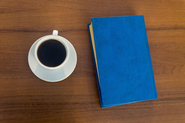 Xícara de café e livro fechado na mesa de madeira. Vista do topo