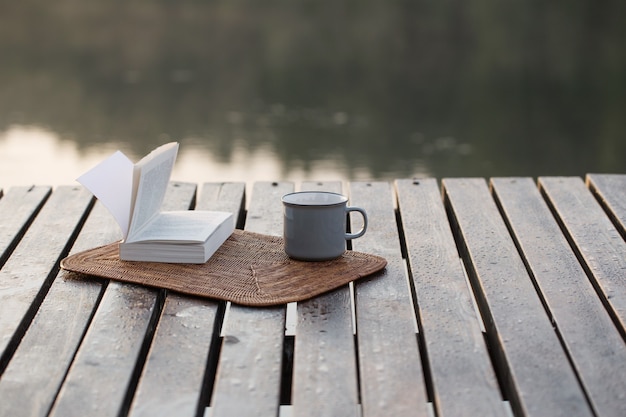 Xícara de café e livro no cais de madeira no lago de verão