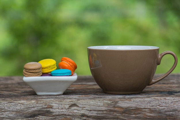 Xícara de café e Macaroons coloridos no prato na mesa de madeira