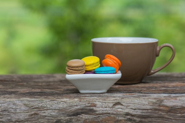 Xícara de café e Macaroons coloridos no prato na mesa de madeira