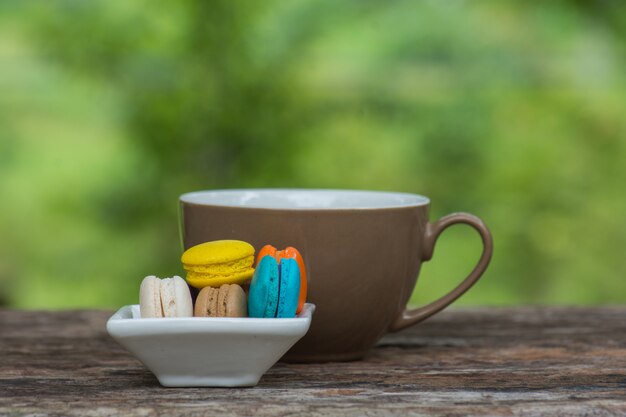 Foto xícara de café e macaroons coloridos no prato na mesa de madeira