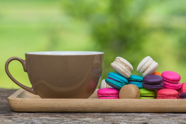 Xícara de café e macaroons coloridos no prato na mesa de madeira