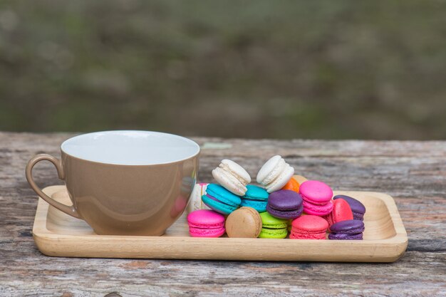 Xícara de café e macaroons coloridos no prato na mesa de madeira