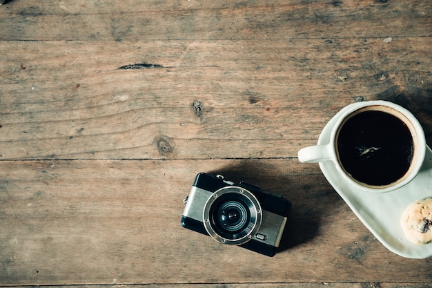 Xícara de café e restro câmera na mesa de madeira com tom vintage