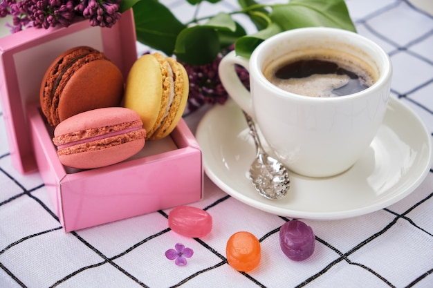 Xícara de café e saborosos macarons doces com caramelo e pirulitos coloridos