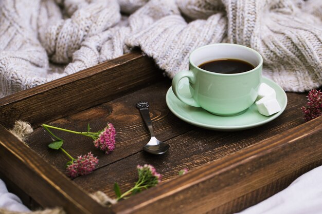 Xícara de café e vela em uma bandeja de servir de madeira rústica e suéter de lã quente de tricô