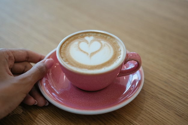 Xícara de café em pé na mesa de madeira. feche a mão segurando uma xícara de cappuccino aromatizado em um café