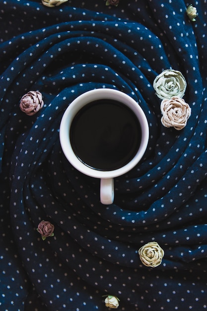 xícara de café em um lenço azul profundo com flores rosas