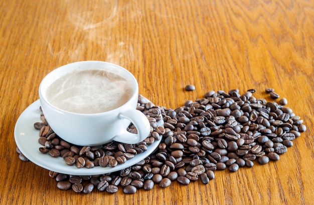 Xícara de café em uma xícara branca e grãos de café na mesa de madeira ba