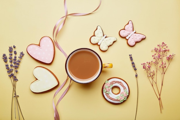 Xícara de café estética e biscoitos entre flores Conceito feminino de café da manhã Dia das mães Dia das mães Cartão de primavera com biscoitos vitrificados assados em fundo amarelo