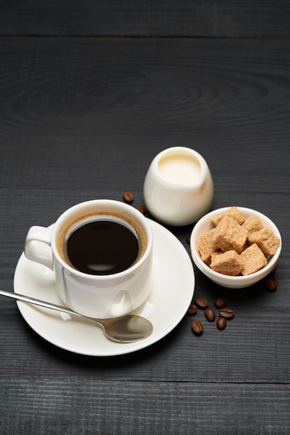 Xícara de café expresso e bule de creme ou leite na mesa de madeira escura