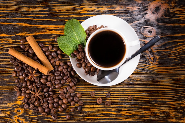 Xícara de café expresso recém-preparada com grãos de café inteiros torrados, hortelã, anis estrelado e especiarias em pau de canela em uma mesa de madeira rústica, vista aérea